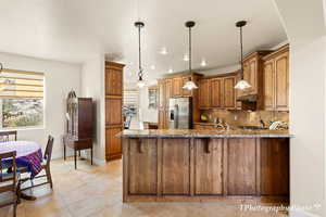 Kitchen featuring pendant lighting, stainless steel fridge, stone countertops, decorative backsplash, and kitchen peninsula