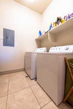 Washroom featuring washing machine and clothes dryer, light tile patterned floors, and electric panel