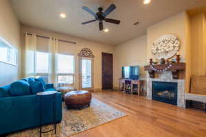 Living room featuring a tiled fireplace, hardwood / wood-style flooring, and ceiling fan