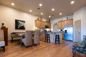 Kitchen featuring appliances with stainless steel finishes, dark stone countertops, a kitchen bar, light hardwood / wood-style floors, and kitchen peninsula