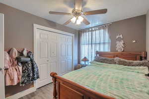 Bedroom with ceiling fan, light hardwood / wood-style floors, and a closet