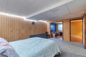 Bedroom with carpet flooring, a paneled ceiling, and wood walls