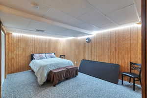 Bedroom featuring carpet flooring, a paneled ceiling, and wooden walls