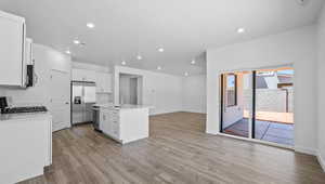 Kitchen featuring an island with sink, sink, white cabinets, stainless steel appliances, and light hardwood / wood-style flooring