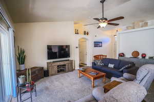 Carpeted living room featuring ceiling fan and vaulted ceiling