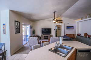 Kitchen with vaulted ceiling, light tile patterned flooring, dishwasher, sink, and ceiling fan