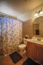 Bathroom featuring tile patterned floors, toilet, tile walls, vanity, and a shower with shower curtain