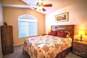 Carpeted bedroom featuring vaulted ceiling and ceiling fan