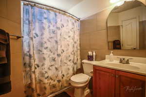 Bathroom with vanity, toilet, a shower with shower curtain, and tile walls