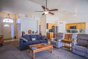 Carpeted living room with ceiling fan and high vaulted ceiling