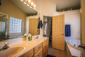 Primary Bathroom  vanity with double sinks, vaulted ceiling, tile patterned floors, and plus walk in shower