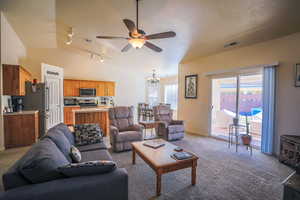 Carpeted living room featuring vaulted ceiling, rail lighting, ceiling fan with notable chandelier, and a textured ceiling