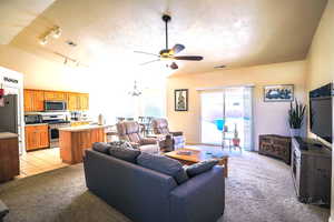 Carpeted living room featuring lofted ceiling, rail lighting, ceiling fan with notable chandelier, and a textured ceiling