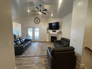 Living room with hardwood / wood-style flooring, a stone fireplace, ceiling fan, and vaulted ceiling