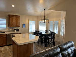 Kitchen with pendant lighting, dishwasher, backsplash, dark hardwood / wood-style floors, and a notable chandelier