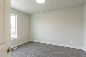 Empty room with baseboards and dark colored carpet