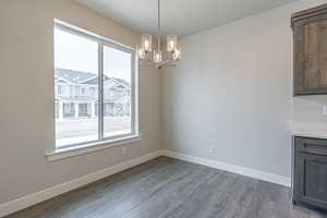 Unfurnished dining area with baseboards, wood finished floors, and a notable chandelier