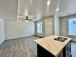 Kitchen with sink, hardwood / wood-style floors, light stone countertops, a textured ceiling, and a center island with sink