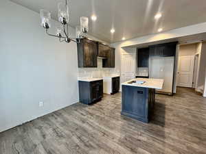 Kitchen with hardwood / wood-style floors, pendant lighting, a center island, dark brown cabinets, and a textured ceiling