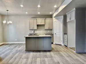 Kitchen with sink, gray cabinetry, light stone counters, and light hardwood / wood-style floors