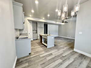 Kitchen featuring sink, a kitchen island with sink, hanging light fixtures, light stone countertops, and light wood-type flooring