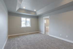 Spare room featuring light carpet, a raised ceiling, a textured ceiling, recessed lighting, and baseboards