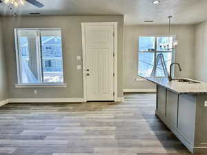 Kitchen with sink, light stone counters, hanging light fixtures, a textured ceiling, and light hardwood / wood-style floors