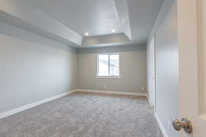Unfurnished room featuring a textured ceiling, a raised ceiling, baseboards, carpet, and recessed lighting