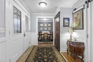 Foyer featuring ornamental molding, light wood-type flooring, and a textured ceiling