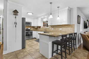 Kitchen featuring pendant lighting, white cabinetry, a breakfast bar area, kitchen peninsula, and stainless steel appliances