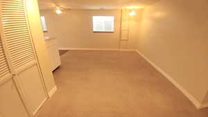 Basement featuring light colored carpet and ceiling fan