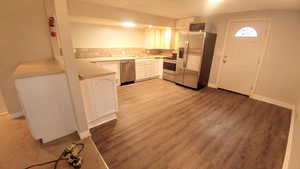 Kitchen featuring appliances with stainless steel finishes, white cabinetry, sink, decorative backsplash, and light wood-type flooring