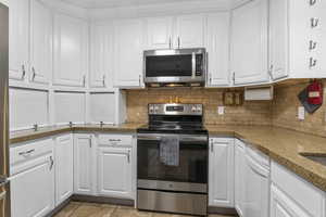 Kitchen featuring white cabinetry, stainless steel appliances, light stone countertops, and tasteful backsplash