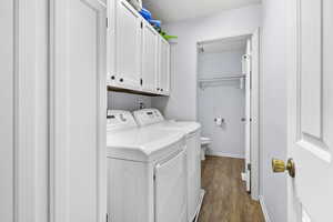 Clothes washing area with cabinets, dark wood-type flooring, and washing machine and clothes dryer