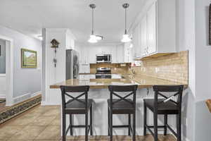 Kitchen with appliances with stainless steel finishes, a breakfast bar, white cabinetry, sink, and kitchen peninsula