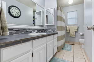 Bathroom featuring tile patterned floors, toilet, decorative backsplash, and vanity