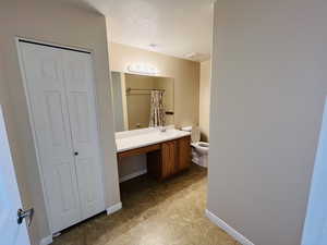 Bathroom with large vanity, a textured ceiling, and toilet