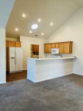 Kitchen with white appliances, lofted ceiling, kitchen peninsula, and mid-color carpet