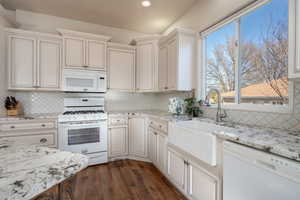 Kitchen featuring dark hardwood / wood-style floors, tasteful backsplash, sink, light stone counters, and white appliances