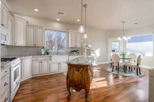 Kitchen featuring white appliances, decorative light fixtures, light stone countertops, and a kitchen island