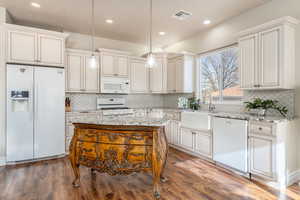 Kitchen featuring a kitchen island, sink, dark hardwood / wood-style flooring, hanging light fixtures, and white appliances