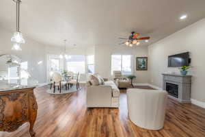 Living room featuring ceiling fan with notable chandelier, dark wood-type flooring, and a healthy amount of sunlight