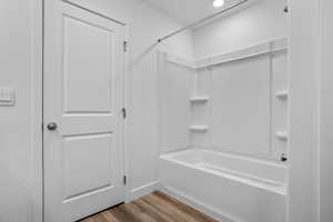 Bathroom with hardwood / wood-style flooring and shower / washtub combination