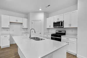 Kitchen featuring dark wood-type flooring, black range with gas cooktop, sink, white cabinetry, and a center island with sink