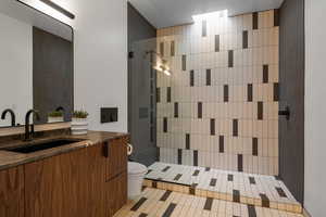 Bathroom with tile patterned floors, vanity, toilet, and a tile shower