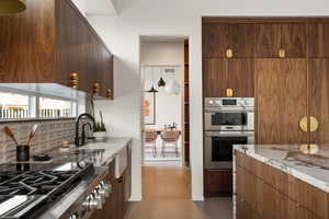 Kitchen featuring sink, light stone countertops, decorative backsplash, cooktop, and stainless steel double oven