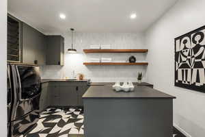 Kitchen with gray cabinets, sink, backsplash, washing machine and clothes dryer, and black fridge