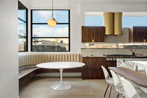 Kitchen with breakfast area, backsplash, light stone counters, dark brown cabinetry, and plenty of natural light