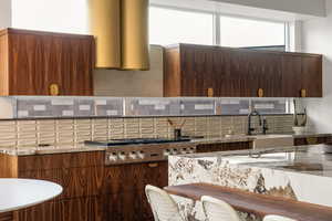 Kitchen featuring sink, backsplash, stainless steel gas cooktop, exhaust hood, and light stone counters