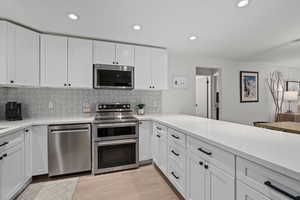 Kitchen featuring tasteful backsplash, white cabinetry, and appliances with stainless steel finishes